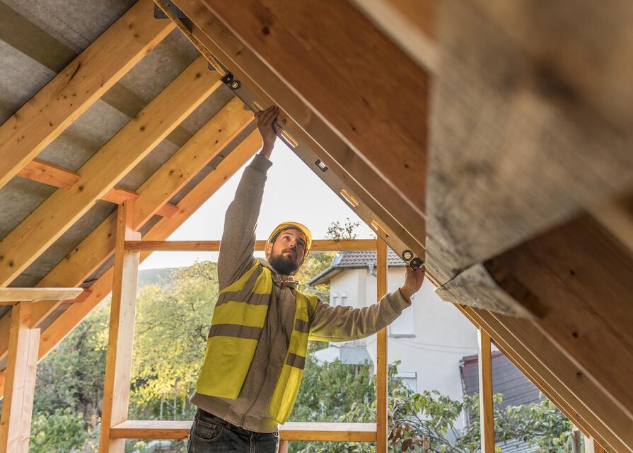 Handwerker prüft mit Wasserwaage die Montage einer Dachkonstruktion aus Holz bei einem Hausbau.